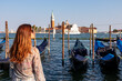 Tourist woman in dress watching gondolas moored by Saint Mark square in city Venice, Veneto, Northern Italy, Europe. Scenic view of San Giorgio di Maggiore church. Romantic vacation in Venetian Lagoon