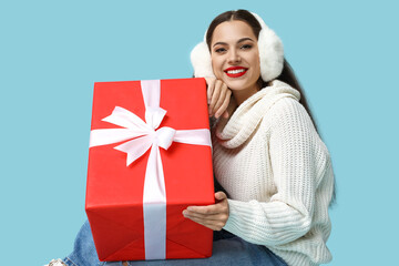 Wall Mural - Beautiful young woman with Christmas gift on blue background