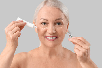 Wall Mural - Beautiful mature woman applying eye cream on light background, closeup