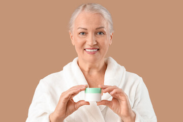 Canvas Print - Beautiful mature woman with jar of cream on brown background, closeup