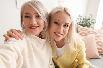 Wall Mural - Mature female friends taking selfie at home, closeup