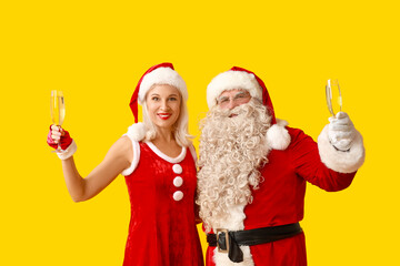 Poster - Santa and MRS Claus with glasses of champagne on yellow background