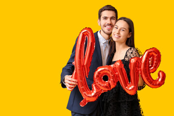 Canvas Print - Beautiful young couple with air balloons in shape of word LOVE on yellow background. Valentine's day celebration