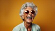 Joyful elderly woman with white hair, laughing heartily behind trendy orange sunglasses, exuding positivity and zest for life against a vibrant orange background