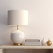 A contemporary white table lamp with golden accents and a linen shade stands beside several volumes on a minimalistic wooden sideboard against a barren beige wall, a mockup.