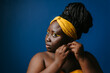 Portrait of beautiful plus size African woman in traditional headwear putting on earrings 