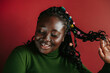 © gstockstudio - Beautiful African woman with braided hair and colorful clips smiling on red background
