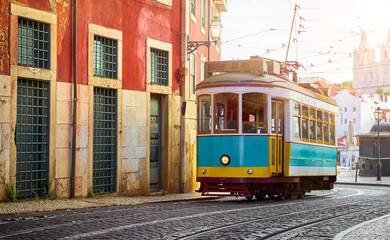 Wall Mural - Lisbon Portugal. Vintage retro tram driving by street of paving stones in district Alfama. Cityscape panorama with old houses and tower sunny day