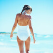© Alliance - Young woman walking at seaside. rear view