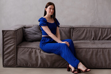 Young beautiful girl in dark blue dress sitting on the sofa