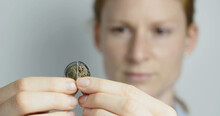 A Young Woman Puts A Broken 2 Euro Coin Together And Smiles At The Camera.