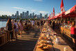 People socializing at a riverfront outdoor dining event during sunset with a city skyline in the background.