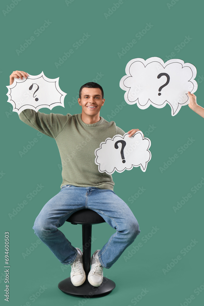 Young man holding speech bubbles with question marks on green background