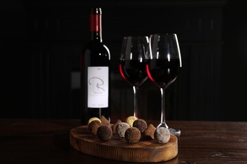 Canvas Print - Red wine and chocolate truffles on wooden table against dark background