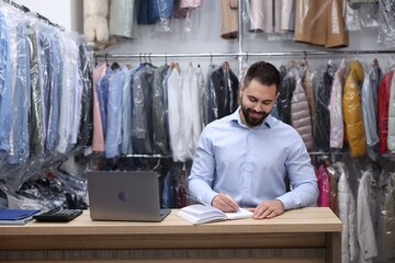 Wall Mural - Dry-cleaning service. Happy worker taking notes at counter indoors