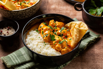 Canvas Print - Indian style dinner. Chicken curry with long rice and naan bread in a dark bowl. Brown table background.