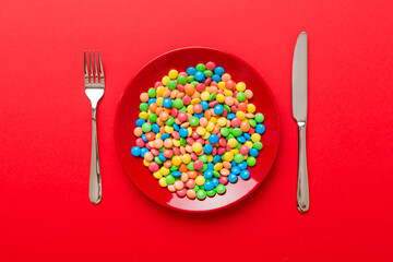 cutlery on table and sweet plate of candy. Health and obesity concept, top view on colored background