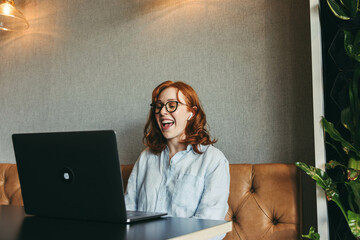 Wall Mural - Ginger-haired businesswoman smiling during a productive online meeting at a cozy café