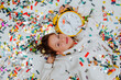 © Westend61 - Smiling girl lying near confetti with clock on floor