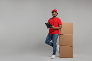 Wall Mural - Happy courier with clipboard and stack of parcels on grey background, space for text