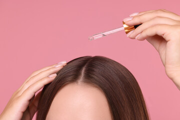 Woman applying serum onto hair on pink background, closeup