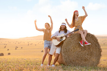 Canvas Print - Beautiful hippie women listening to their friend playing guitar in field, space for text