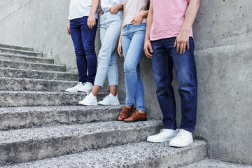 Wall Mural - Group of people in stylish jeans on stairs near stone wall outdoors, closeup