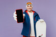 © ViDi Studio - Happy man wear warm blue windbreaker jacket ski goggles mask hat hold snowboard use blank screen mobile cell phone spend extreme weekend winter season in mountains isolated on plain purple background.