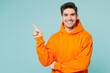 Young smiling happy fun man he wears orange hoody casual clothes point index finger aside on area mock up isolated on plain pastel light blue cyan color background studio portrait. Lifestyle concept.