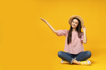 Wall Mural - Young girl with a straw hat on a yellow background