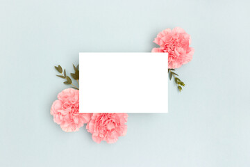 Wall Mural - blank paper card mockup, pink carnation flowers and green eucalyptus branches on a blue background. 
