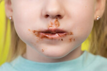 Little Girl's Mouth Dirty With Chocolate On A Yellow Background. Concept Of Children With A Sweet Tooth, Close-up