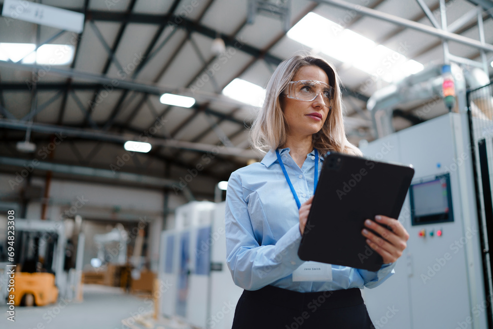 Female manager standing in modern industrial factory. Manufacturing facility with robotics and automation. Female leader, CEO in heavy industry, manufactury.