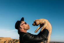 Joyful Moment As Man Lifts Dog Against Blue Sky
