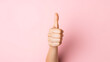 Female hand showing thumbs up sign on a pink background. 