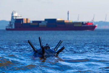 Underwater bomb near ship with containers. Ocean mine for organizing naval blockade. Underwater bomb threatens private vessel. Surfaced bomb from war of last century. Sea mine over water