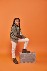 Wall Mural - cheerful preadolescent african american girl in warm outfit posing and smiling happily at camera