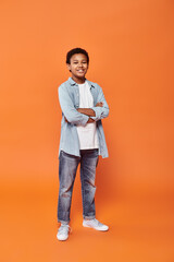 Wall Mural - cheerful african american boy posing joyfully with arms crossed on chest on orange backdrop