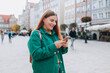 © mdyn - Happy cheerful young woman with backpack walking on city street checks her smartphone. Portrait of beautiful 30s girl using smartphone outdoors. Urban lifestyle concept.