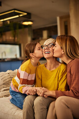 Wall Mural - Three generations, focus on the smiling grandma, getting kisses from her grandchild and her daughter.