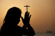 © robertharding - Silhouette of faithful woman praying with Christian cross at sunset as concept for religion, faith, prayer and spirituality, Dubai, United Arab Emirates