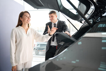 Wall Mural - Cheerful woman buyer choosing car with help of salesman of dealership