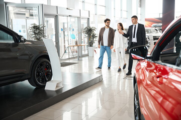 Man and woman choosing and buying car at auto showroom with salesman help