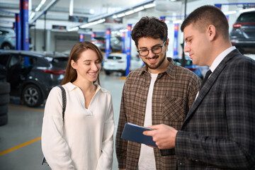 Wall Mural - Car explaining to couple all pros and cons of brand new car at the dealership