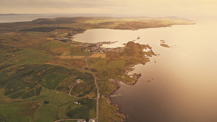 Wall Mural - Countryside pier town cityscape at sunset aerial. Nobody nature landscape. Rural farmlands fields, forest at sun ocean coast. Road at seascape. Ellen Port, Islay Island, United Kingdom, Europe