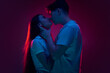Boyfriend and girlfriend, young man and woman kissing against purple background in neon light. Concept of romance, love, relationship, passion, youth, dating, happiness