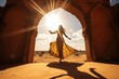 Beautiful young woman in traditional Indian tribal dress dancing on the sand near ancient arch, sunset and desert background.