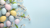 Fototapeta  - Flat lay of pastel-colored Easter eggs interspersed with blossoming branches on a light blue background