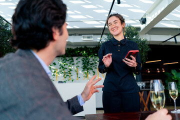 Wall Mural - young smiling waitress girl taking orders from guests writing on the phone concept of hospitality and service in a high class restaurant