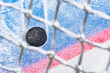 Looking through the net at an ice hockey puck stopping on the edge of the Goal Line of the goal crease.